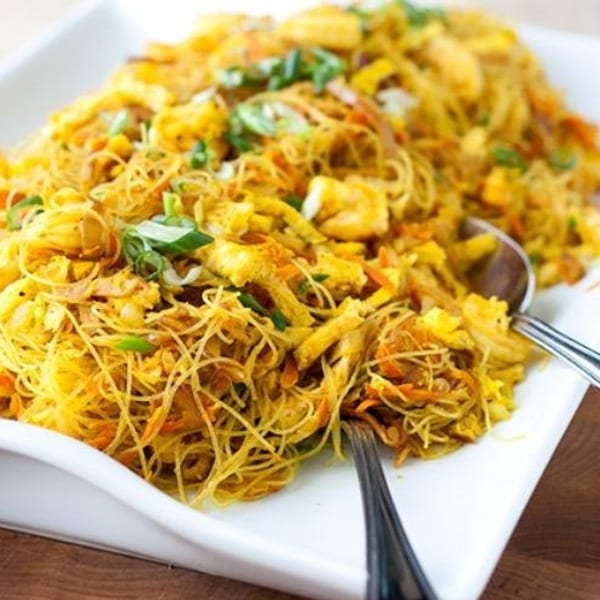 A white rectangular platter filled with Singapore noodles, shrimp, scrambled egg, and green onions.