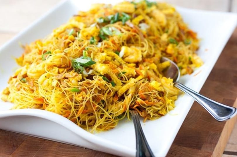 A white rectangular platter filled with Singapore noodles, shrimp, scrambled egg, and green onions.